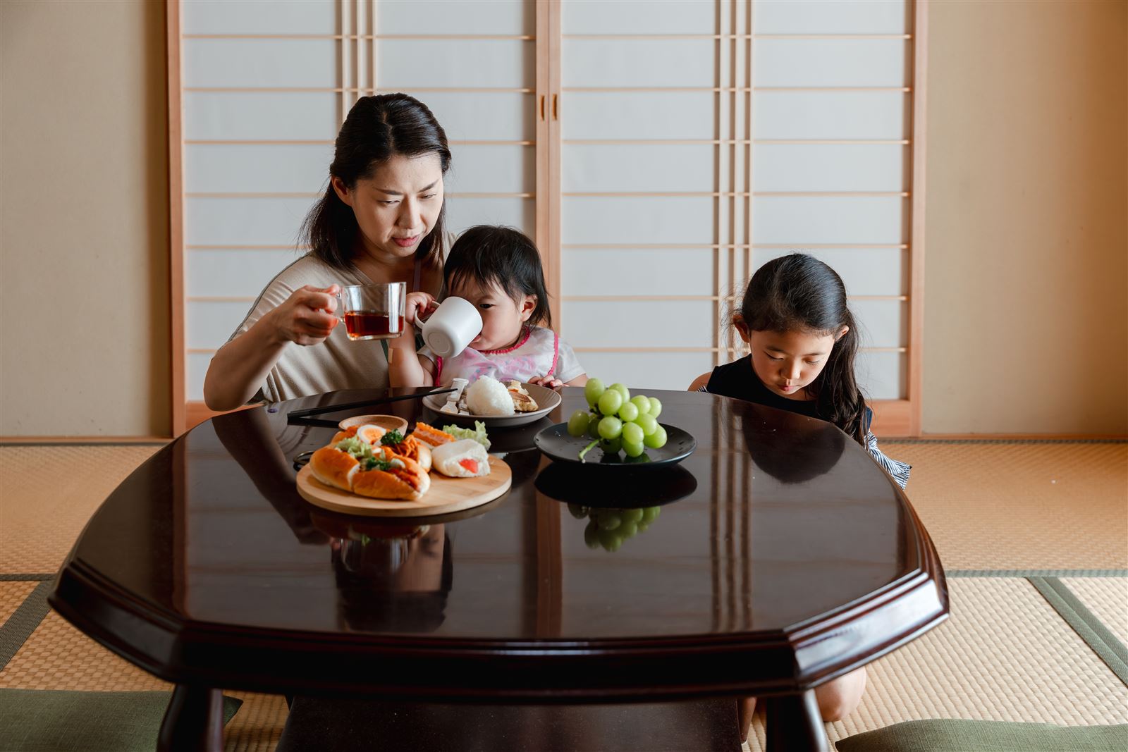 和室の座卓で、お母さんと子どもたちがおやつを食べている